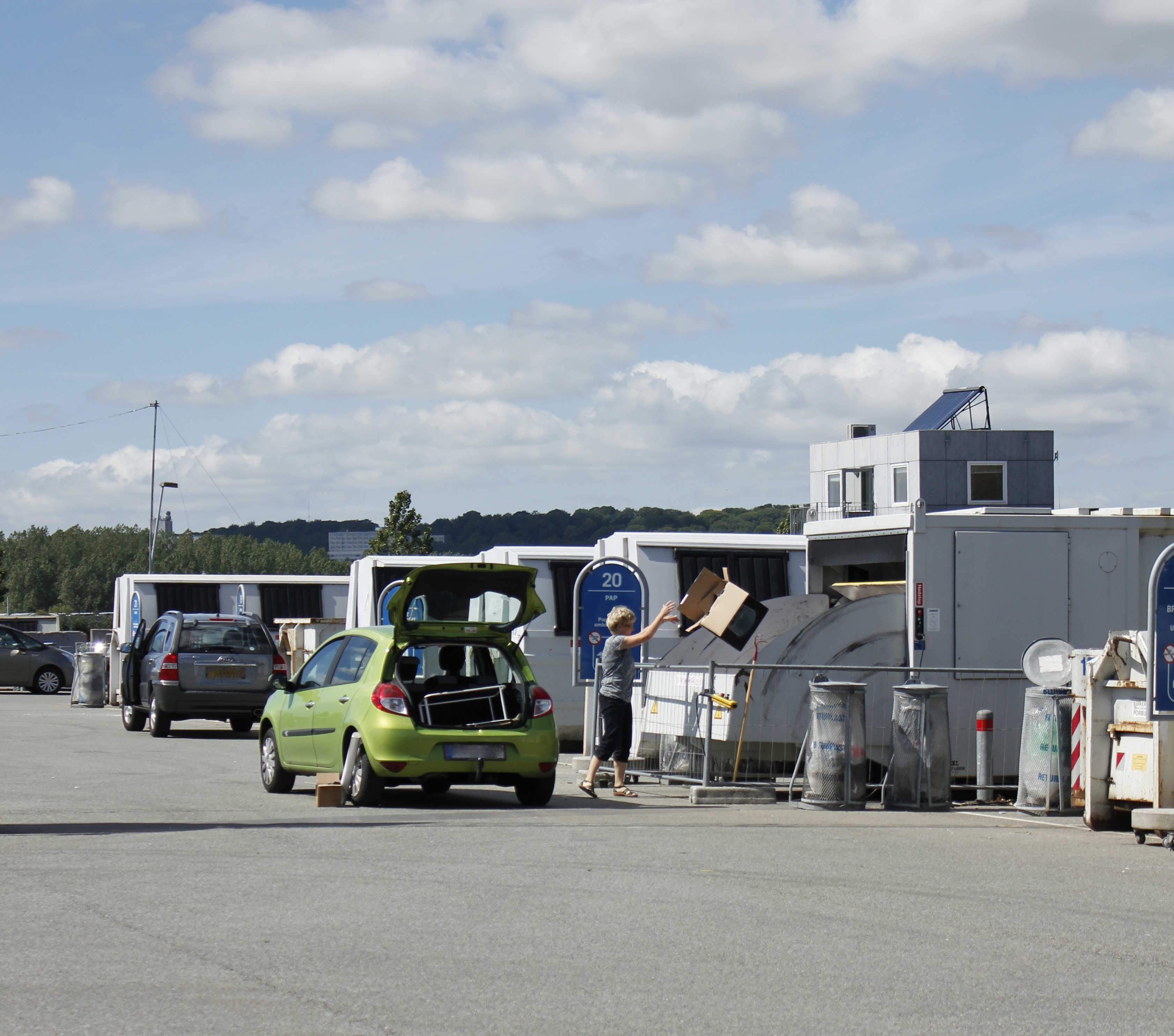 Kvinde smider papkasse i container på genbrugspladsen