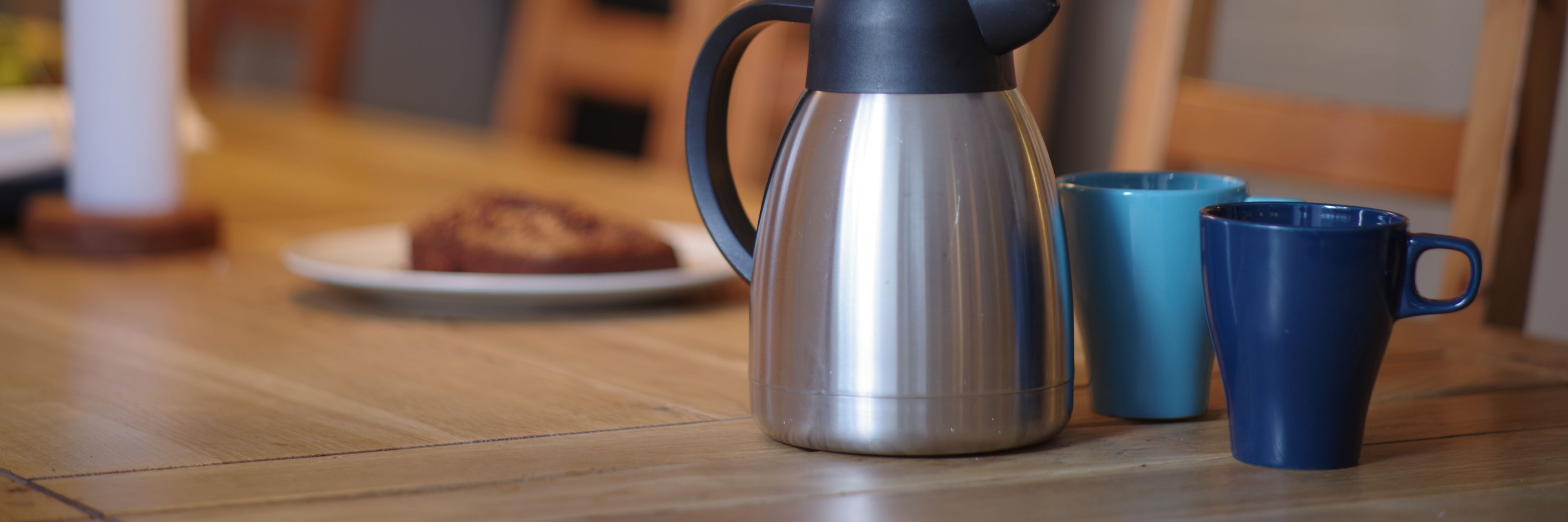 Kaffekande, to blå krus og tallerken med kage på bord